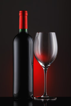  Bottle of red wine with an empty glass on a black background, vertical close-up image