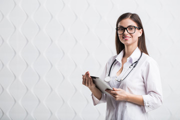 Female brunette doctor wears glasses using tablet, intelligent and lovely woman with the gadget and stethoscope in the white background