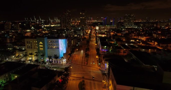 Aerial pull out shot reveal Miami Beach 5th Street night drone video