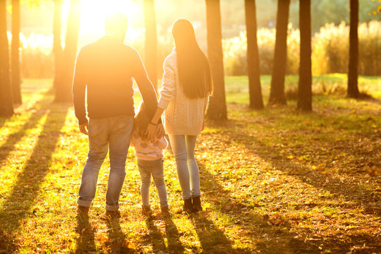 .family with little daughter spend fun time in autumn park at sunset, back view