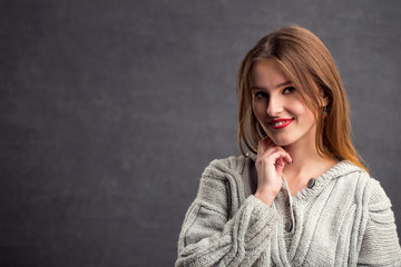 Portrait of beautiful girl in gray sweater, indoor shot in the gray background