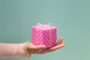 Woman's hand holding pink gift box in polka dots
