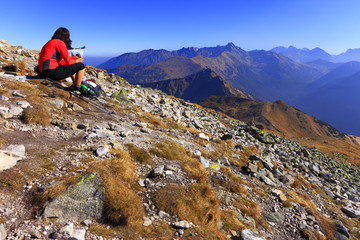Fototapeta premium Zakopane, Tatra Mountains / Poland - 2010/07/04: Tourist resting on a trekking track from Czerwone Wierchy Peaks towards Kasprowy and Swinica Peaks peaks with Western Tatra in background