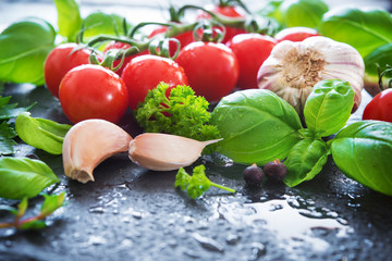 Ripe tomatoes with fresh basil, garlic and other herbs with water drops on slate plate