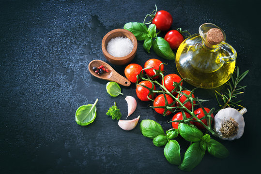 Olive oil, tomatoes, garlic, parsley, basil, spices on dark background with water drops