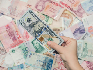 Female hand holding american hundred dollar bills over Asia money background.  World Markets and Trade.