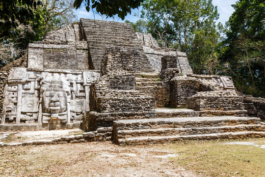 Old ancient stone Mayan pre-columbian civilization pyramid with carved face and ornament hidden in the forest, Lamanai archeological site, Orange Walk District, Belize