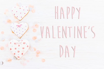 happy valentine's day text sign flat lay. pink cookie hearts and confetti on white rustic wooden background. space for text. greeting card concept. valentines bright image