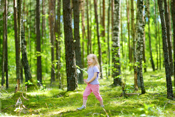 Cute little girl having fun during forest hike on beautiful summer day