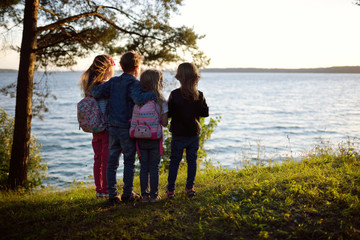 Fototapeta premium Four cute little sibling standing by the lake enjoying beautiful sunset view. Children exploring nature.