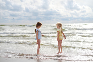 Two little sisters having fun on a sandy beach on warm and sunny summer day. Kids playing by the ocean.