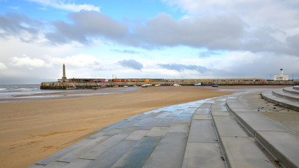 The beach at low tide by stormy and windy weather with Margate Harbor Arm in the background, Margate, Kent, UK