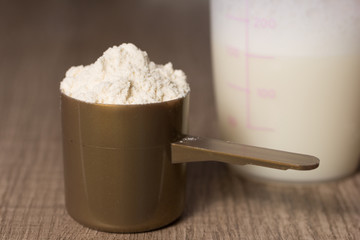 Whey Protein. Golden scoop with vanilla flavour powder, shaker. Wooden table. Close up, texture.
