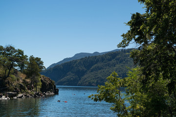 Landscape of a lake with an island, people swimming and mountains in the background