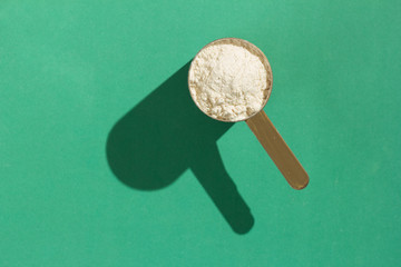 Whey Protein. Minimalism and hard light. Measuring scoop full with vanilla flavour powder on green background.