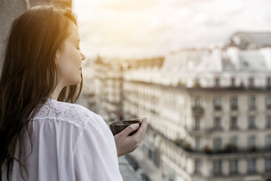 Picture of a young beautiful woman enjoying a cup of tea in the morning on a balcony in France