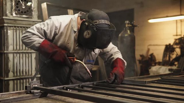 portrait of a professional master in a protective helmet that covers his eyes, the worker is engaged in welding metal sticks in a modern workshop