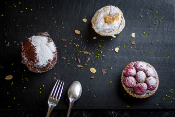 assorted desserts on black plate raspberry tart cream cake paris brest and chocolate cake 