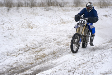 Sportsman racer man fulfills a fast ride on a motorcycle on the road extreme. The race track is very uneven. Cloudy winter day with a snowstorm.