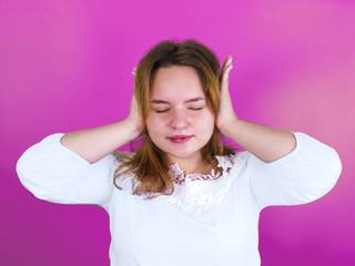 Annoyed young woman in white blouse covering her ears with her hands
