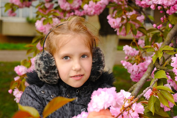 Fototapeta premium The young girl stands next to the blooming sakura in the spring