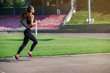 Young fitness woman running on a stadium track. Athlete girl doing exercises on the training at stadium. Healthy active lifestyle.