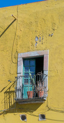 Exterior of an old house with a bright yellow wall, small balcony with a double french door with a stone door frame, plants in clay pots and a sliver of  blue sky, in Guanajuato, Mexico - 191672374