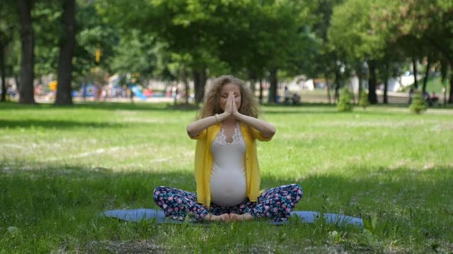 Beautiful pregnant woman doing prenatal yoga on nature outdoors. Sport, fitness, healthy lifestyle while pregnancy. Pregnant woman practicing yoga pose, breathing exercise, stretching in summer park.