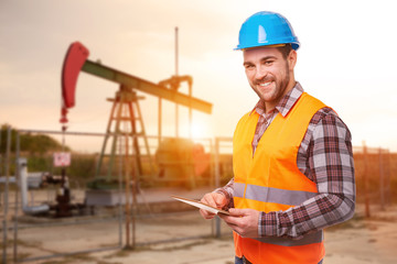 Refinery worker with tablet standing in front of the oil pump