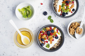 Yogurt, milk porridge, granola for breakfast with different berries, nuts and fruits: kiwi, pomegranate, dried apricots, blueberries, almonds and honey. Portionally. Top view Food concept.