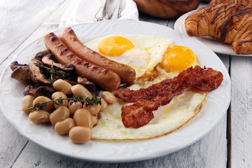 Traditional full English breakfast with fried eggs, sausages, beans, mushroomsand bacon on wooden background