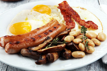 Traditional full English breakfast with fried eggs, sausages, beans, mushroomsand bacon on wooden background
