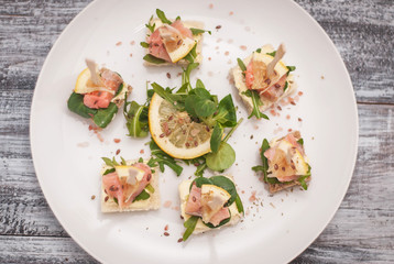 Canapes with Salmon fish and Arugula Leaves and Butter Cream. top View. White Plate on Wooden Gray Background.