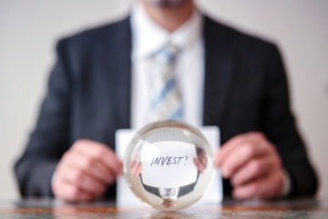 man holding paper with word Invest in front of glass ball