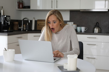 Hübsche blonde Frau sitzt vor einem Laptop und ist erstaunt