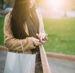 young trendy woman in autumn city park with smartphone in hand