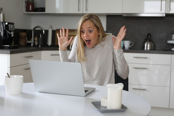 Hübsche blonde Frau sitzt an einem Laptop begeistert
