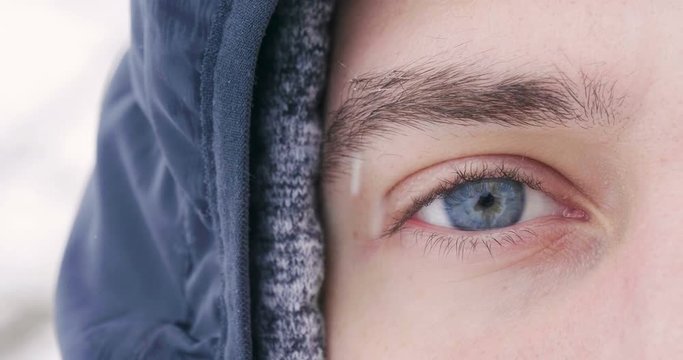 Close up of a blue eye of a man watching in the room while the snow falls from the sky in slow motion. Concept of: nature, eyes, magic moment, winter holidays