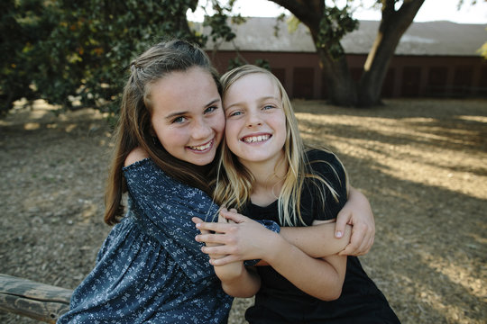 Portrait of cheerful sisters embracing at farm