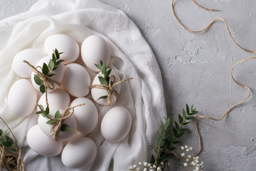 Fototapeta na wymiar Easter concept. White chicken eggs on white fabric. Decorated with eucalyptus leaves. Top view and copy space.