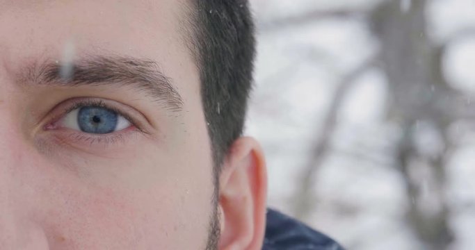 Close up of a blue eye of a man watching in the room while the snow falls from the sky in slow motion. Concept of: nature, eyes, magic moment, winter holidays