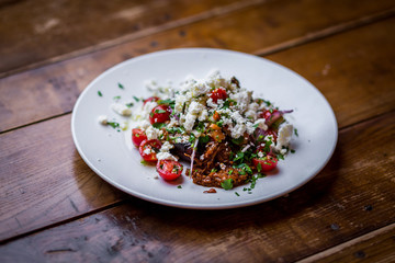 home made feta salad with tomatoes on white plate on wooden table 