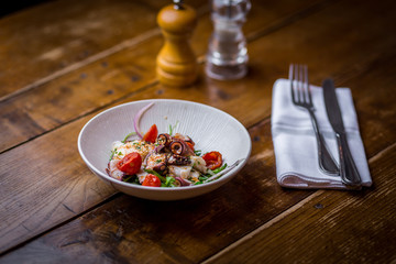 calamari salad with fresh vegetables in white plate on wooden table