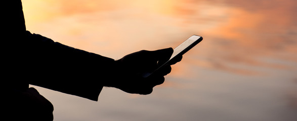 The panorama of  woman is standing near the water, using smart phone and waiting someone, side view