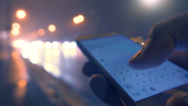 Close up shot of a male hand using smartphone on the city street at night with a blurred city lights on the background 