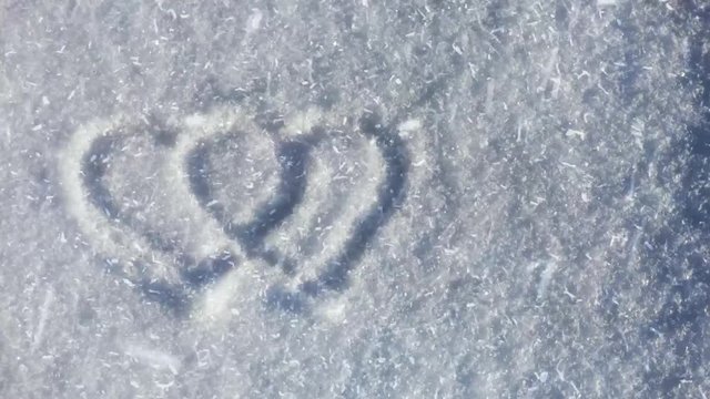 Two heart symbols on the snow. Lot of snowflakes flying on the wind. Romantic sign silhouette on winter ground. Valentines day natural background.