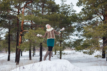 Portrait of beautiful attractive girl outdoors in winter forest. Slender attractive girl on a background of pines in the winter, looks away and smiles. Space.