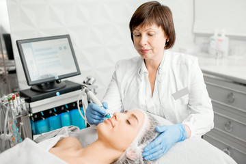 Senior woman cosmetologist making facial procedure to a young client in a luxury medical resort office