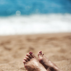 Female feet with manicured nails on the beach against the sea.