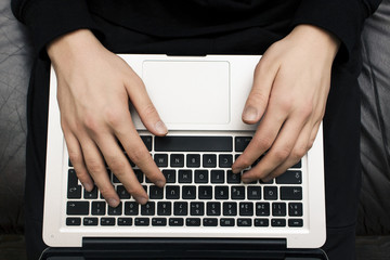 Fototapeta na wymiar Man's hands typing on laptop on the knees on sofa. Freelancer concept